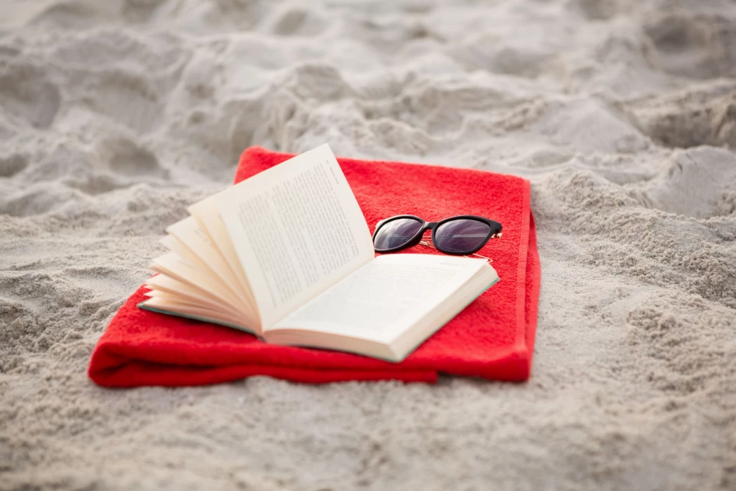 ouvrir-le-livre-et-des-lunettes-de-soleil-conserves-sur-la-serviette-rouge.jpg