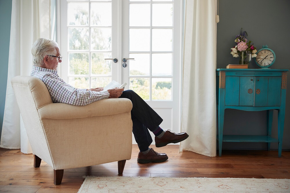 Homme senior lisant un livre dans son fauteuil à la maison 